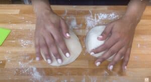 Hands kneading dough on a floured wooden surface, preparing for baking homemade bread.